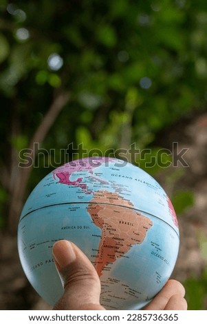 hand holding a terrestrial globe with green texture background  showing South and North america