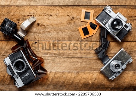 vintage photo cameras, negatives and slides on a textured wooden table. View from above. retro style. Space for text.