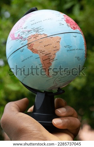 hand holding a terrestrial globe showing South America with green background