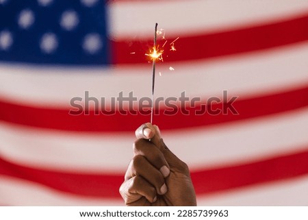 Hand of biracial man holding sparkler and flag of united states of america with copy space. American patriotism, independence day and tradition concept.