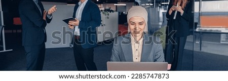 Smiling muslim businesswoman in hijab working on computer while sitting in modern office