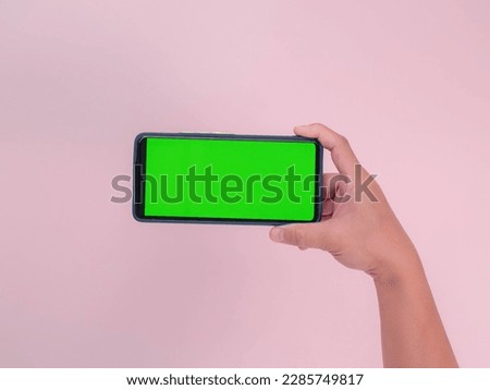 Human hand holding mobile smartphone with green screen in horizontal position isolated on pink background. clipping path