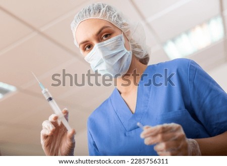 European female doctor in face mask preparing syringe for vaccination in hospital