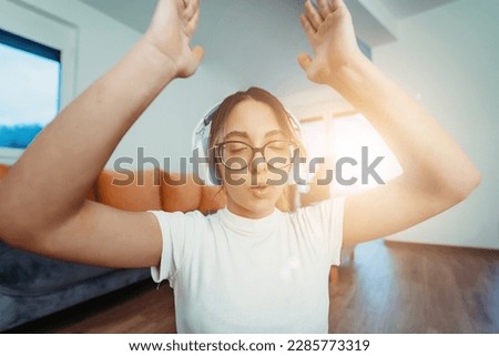 A young woman is practicing yoga and relaxing with headphones on her head in a modern apartment