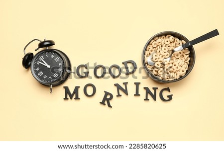 Composition with text GOOD MORNING, alarm clock and bowl of cereal rings on color background