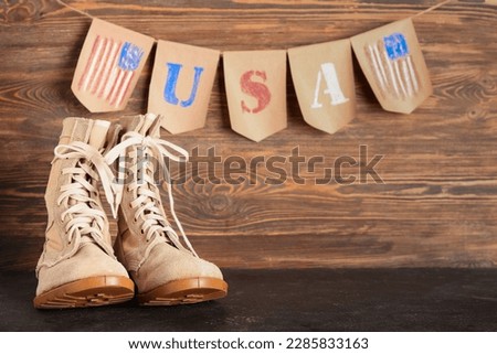 Military boots and garland in colors of USA flag on black grunge table