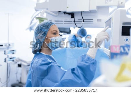 Portrait of a young female doctor in scrubs and a protective face mask preparing an anesthesia machine before an operation Royalty-Free Stock Photo #2285835717