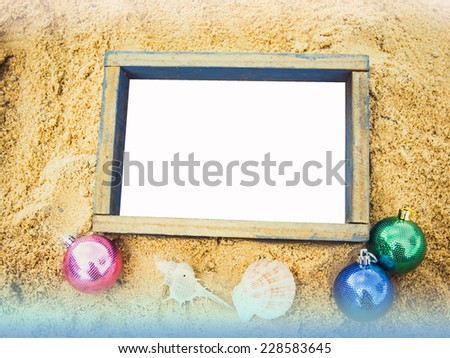 vintage style empty photo frame and Christmas ball lying on a sea sand background. Space for your text.