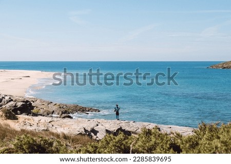 Man wearing sports clothes and carrying a backpack takes pictures of the Atlantic coastline near Porto Covo, Portugal. Capturing moments on a mobile phone.