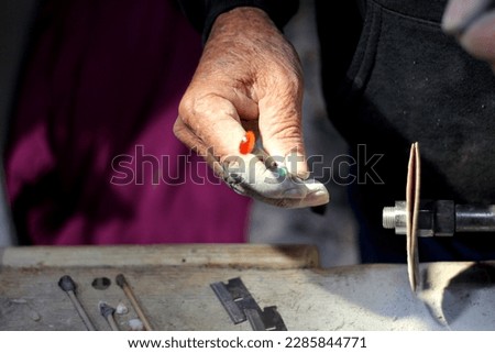 Hands of elderly craftsman man working in a workshop polishing opal stones and minerals to form precious jewelry