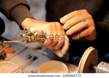 Hands of elderly craftsman man working in a workshop polishing opal stones and minerals to form precious jewelry