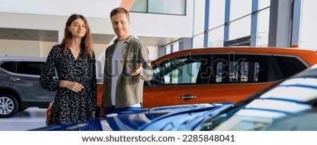 Buying a dream car. A man and a young woman walk around a car dealership and choose the color of the future car. Panoramic photography