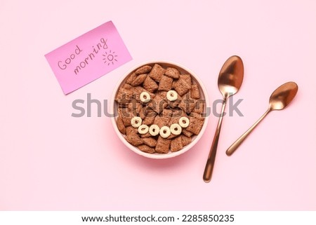 Bowl of tasty corn pillows, spoons and paper with text GOOD MORNING on pink background