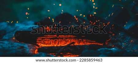 Vivid smoldered firewoods burned in fire close-up. Atmospheric background with orange flame of campfire and blue smoke. Warm full frame image of bonfire. Glowing embers in air. Bright sparks in bokeh Royalty-Free Stock Photo #2285859463