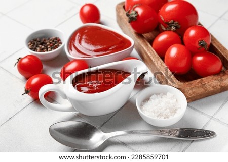 Gravy boat with tasty ketchup and fresh tomatoes on white tile background