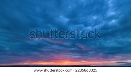 Dramatic sunset, aerial, panoramic photography, minimal horizon. Orange and blue-purple shades of colours, a ray of sunlight penetrating the clouds. Ideal for sky replacement projects.