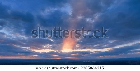 Dramatic sunset, aerial, panoramic photography, minimal horizon. Orange and blue-purple shades of colours, a ray of sunlight penetrating the clouds. Ideal for sky replacement projects.