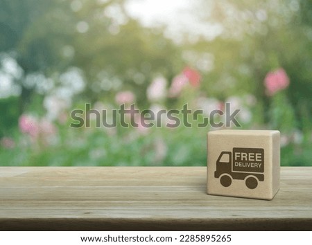 Free delivery truck icon on wood block cube on wooden table over blur pink flower and tree in park, Business transportation service concept