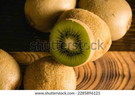 Sweet fruit on a dark background. Half kiwi macro and whole fruit on wooden cutting board.