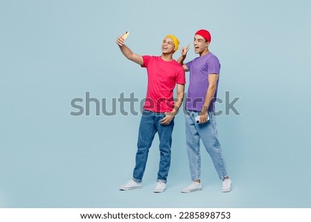 Full body happy smiling young couple two friends men wear casual clothes together doing selfie shot on mobile cell phone show v-sign isolated on pastel plain light blue cyan background studio portrait