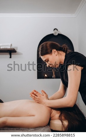 Anonymous female masseur pressing on back of client with elbows while doing traditional massage in light modern clinic.