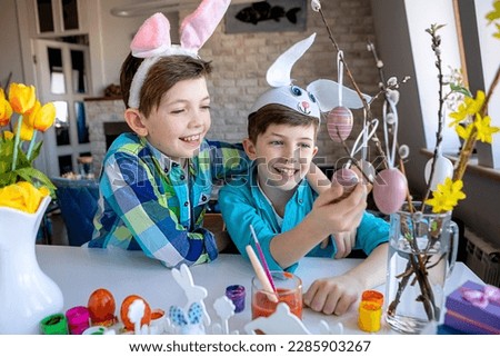 easter concept. Cute little boys decorate pussy willow twigs with hanging easter eggs indoors