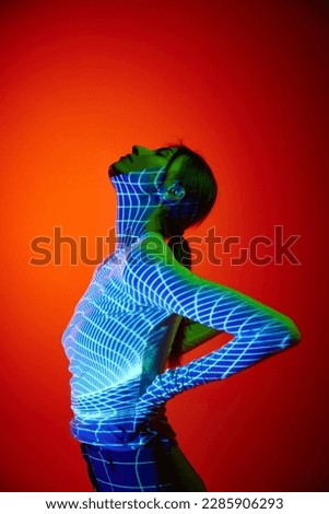 Young beautiful woman's portrait with digital neon filter lights on body over red background. Concept of art, fashion, cyberpunk, futurism and creativity. Projector light illumination on body