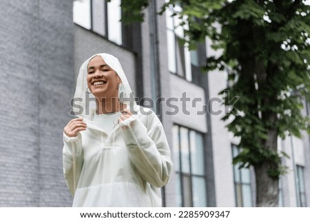 carefree african american woman in waterproof raincoat standing under rain outdoors