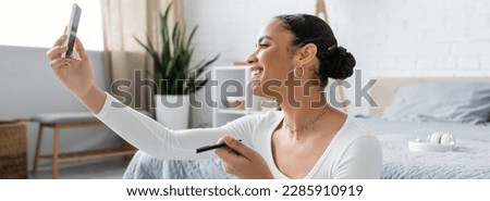 happy african american woman taking selfie on smartphone in modern bedroom, banner