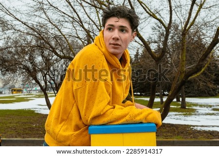 A teenager in a yellow wet and dirty hoodie standing outside on a gloomy, rainy day. Street photo.