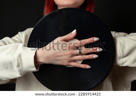 Charming happy young redhead girl in a white oversized sweatshirt holds a vinyl record. Isolated on black.