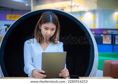 Beautiful asian business woman sitting on a round chair holding a tablet with a focused expression on her face, Digital marketing.