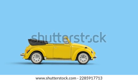 Model of yellow retro toy car cabriolet on solid blue background. Miniature car side view with copy space