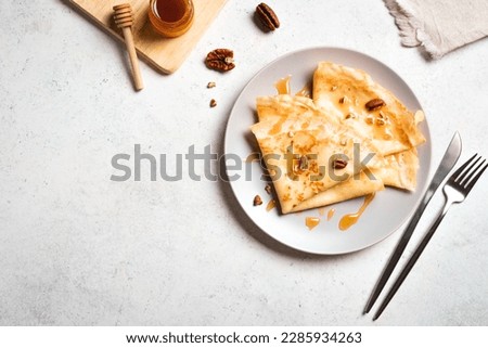 Crepes Suzette with honey and pecan nuts on white background, copy space. Delicious homemade Crepes for breakfast. Royalty-Free Stock Photo #2285934263