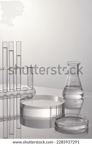 Lab theme with lab glassware and transparent podium on white background. Test tubes, petri dish and erlenmeyer flask filled transparent liquid. Space for display product. Royalty-Free Stock Photo #2285937291