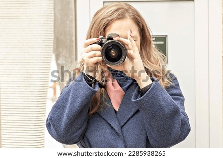 A female photographer with a camera in her hands takes a picture. Paparazzi with a camera in their hands in nature, in the city.