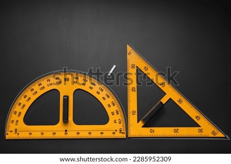 Protractor, triangle ruler and chalk on black table, flat lay. Space for text