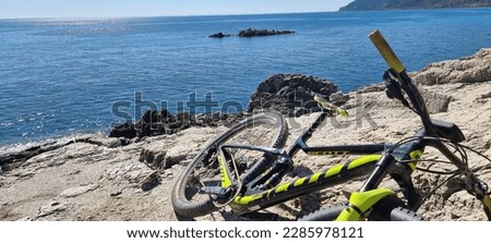 In this picture, we see an individual using a mountain bike to stay fit and active on an island. The scenery around the rider is breathtaking, with a mix of sandy beaches and towering mountains i