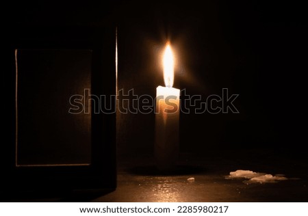 Burning candle on blurred dark background with an empty wooden frame in foreground close up