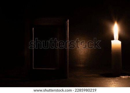 Image with dark candle lighting. Wooden frame for a photo or image on blurred dark background with burning candle