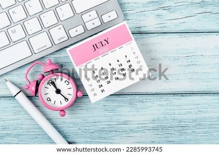 July 2023 Monthly calendar year and alarm clock with keyboard computer on wooden background.