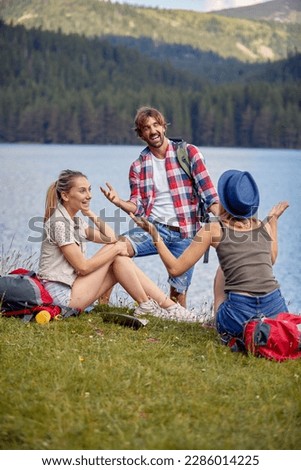 A group of friends chatting while taking a rest at the lake during mountain hiking on a beautiful day. Trip, nature, hiking Royalty-Free Stock Photo #2286014225