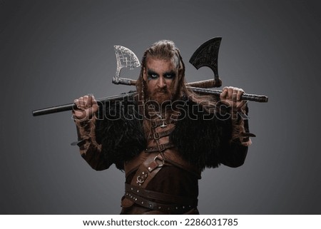 Shot of medieval nordic barbarian with black fur and armor holding two axes. Royalty-Free Stock Photo #2286031785