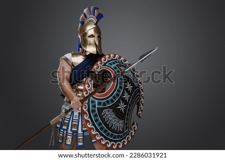 Shot of greek soldier dressed in helmet and armor holding long spear and rounded shield.