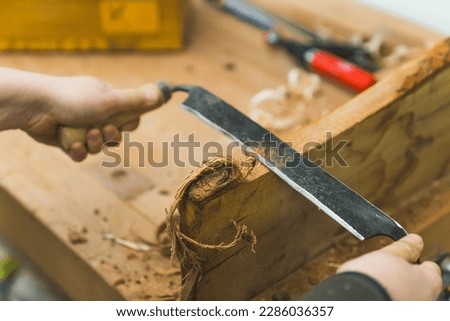 Shaping wood concept. Professional woodworker using drawshave with both hands to shape piece of wood. Closeup shot. High quality photo