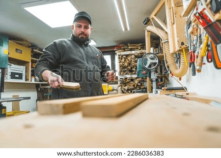 Woodworking artistry concept. Adult craftsman preparing wooden planks to be used. Low angle indoor shot. Carpentry garage. High quality photo