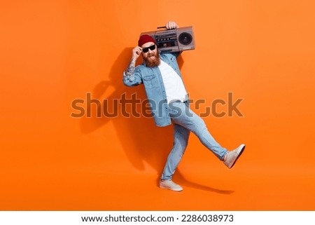 Full length photo of confident cool man wear jeans shirt dancing listening boom box isolated orange color background