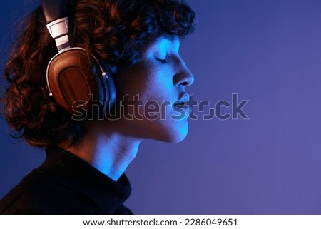 Man wearing headphones listening to music with his eyes closed, enjoying the sound, hipster lifestyle blogger, portrait purple background, mixed neon light, fashion style and trends, copy space Royalty-Free Stock Photo #2286049651