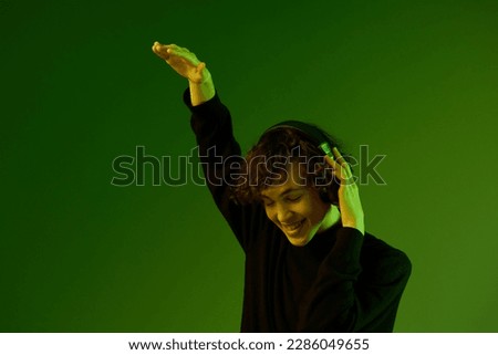 Man wearing headphones listening to music and dancing, DJ happiness and smile laughter, hipster teen lifestyle, portrait green background mixed neon light, copy space