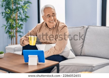 Senior man drinking coffee watching touchpad at home